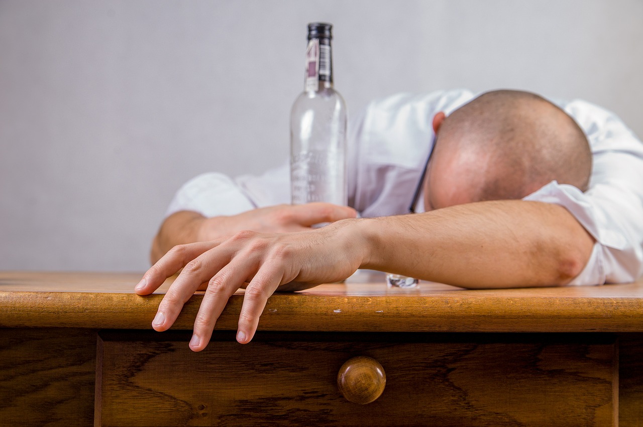 Man experiencing a hangover laying on a table with a bottle of alcohol