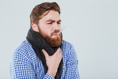 man suffering from a cold with a thermometer in his mouth