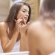 woman looking in mirror popping a pimple