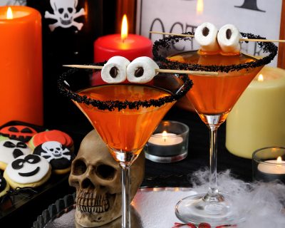 glass of citrus martini decorated with black sugar with marshmallow eyes on the table in honor of Halloween